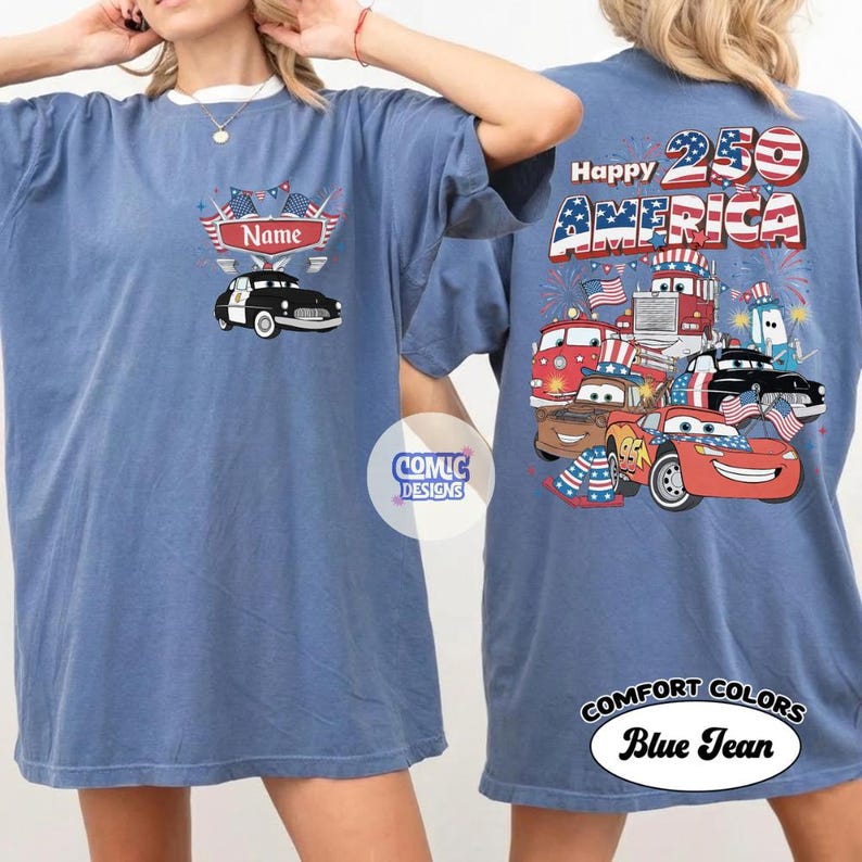 May include: Blue jean Comfort Colors t-shirt with a patriotic design. The front features a police car graphic with space for a name. The back displays "Happy 250 America" with cartoon vehicles and fireworks.