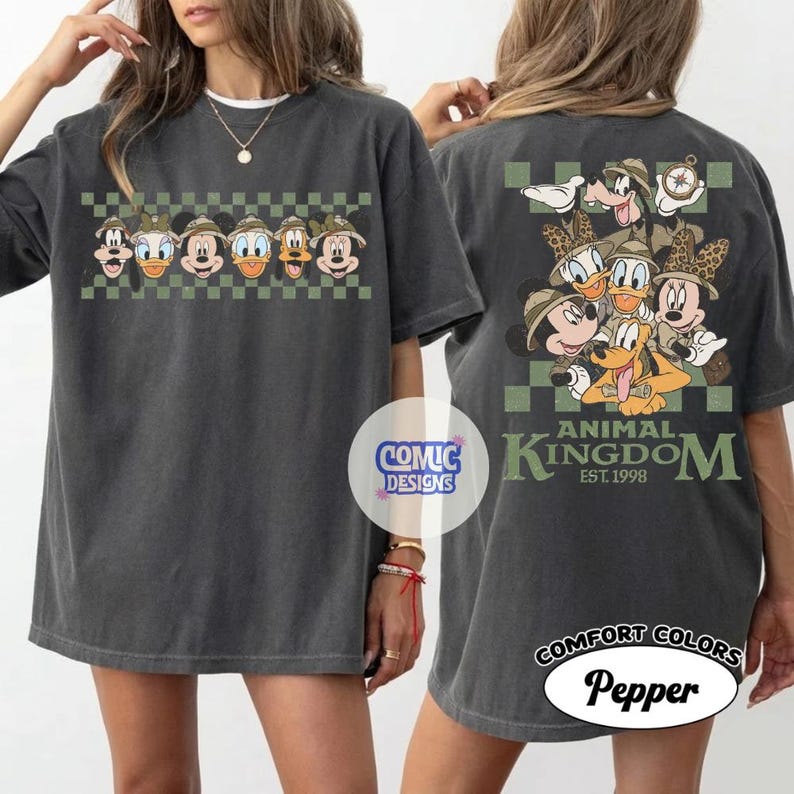 Pode incluir: Camiseta cinza escuro com personagens da Disney usando chap&eacute;us de safari. A frente mostra uma fileira de personagens, a parte de tr&aacute;s um grupo com "Animal Kingdom" e "Est. 1998". A camiseta &eacute; rotulada como "Comfort Colors Pepper".