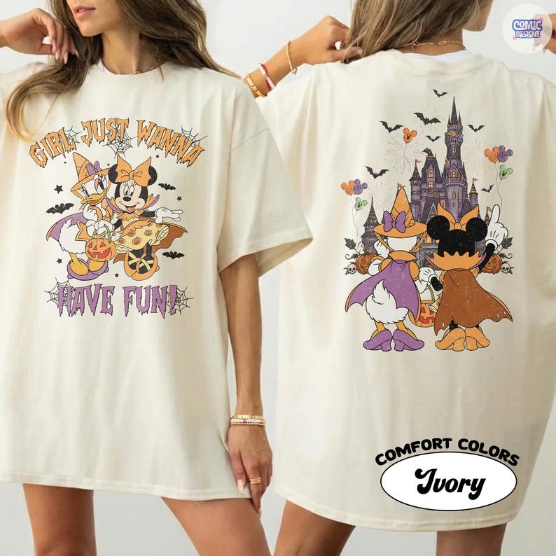 May include: An ivory t-shirt featuring a Halloween-themed graphic. The front displays Daisy Duck and Minnie Mouse with the text "GIRL JUST WANNA HAVE FUN!" The back shows the characters facing a castle with bats, balloons, and pumpkins.