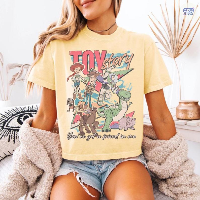 Może przedstawiać: Jasnoż&oacute;łta koszulka z grafiką z filmu Toy Story. Projekt zawiera postacie takie jak Woody, Buzz Lightyear i Rex, z tekstem "TOY STORY" i "You've got a friend in me".