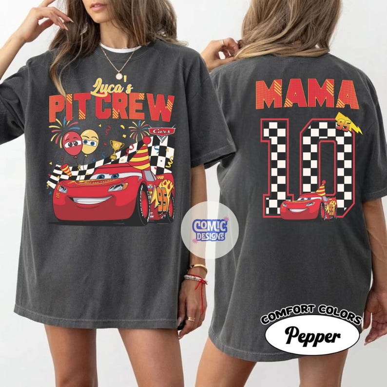 May include: Dark gray t-shirt featuring a red race car graphic with the text "Luca's PIT CREW" on the front. The back of the shirt displays "MAMA" above a checkered number 10 and a smaller car graphic. The shirt is labeled "Comfort Colors Pepper".