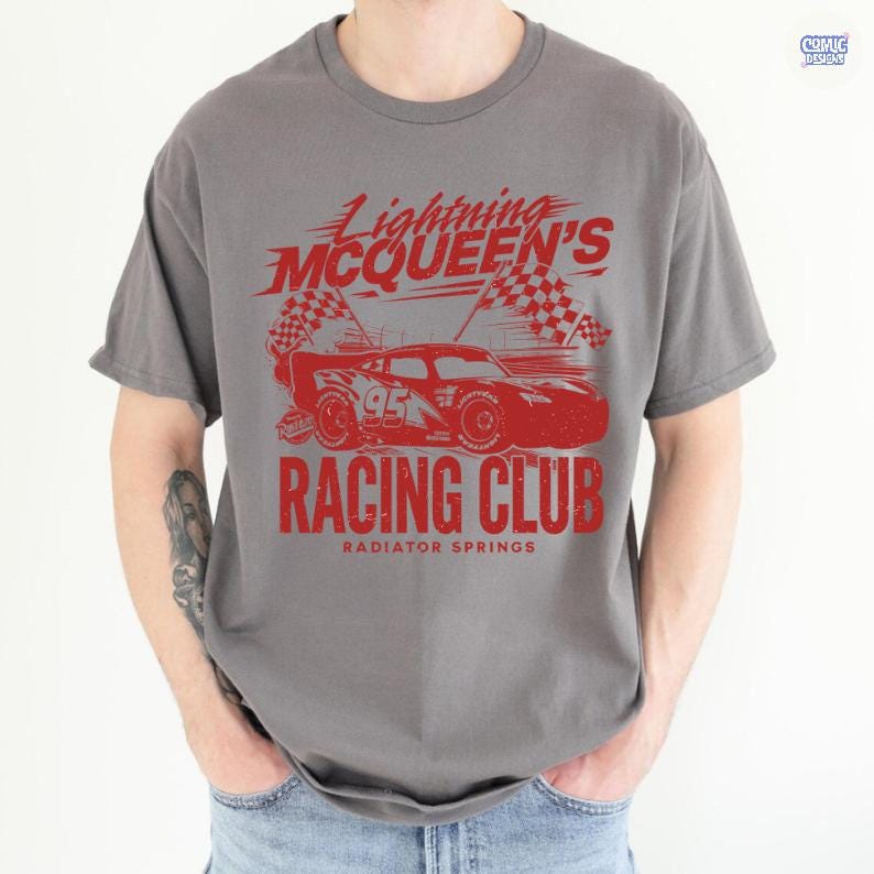 May include: Gray t-shirt featuring a red graphic of Lightning McQueen's Racing Club. The design includes a race car, checkered flags, and the text "Lightning McQueen's Racing Club, Radiator Springs". The shirt has short sleeves and a crew neck.