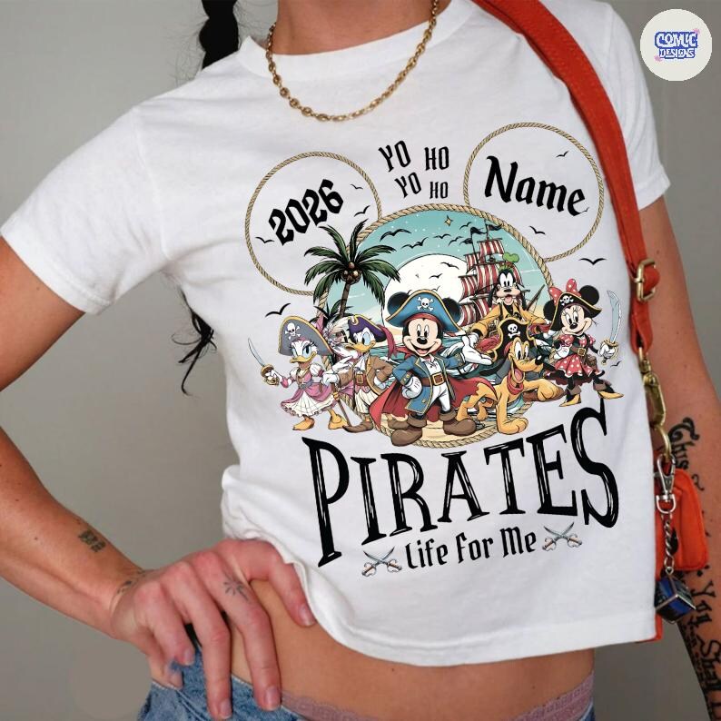 May include: White t-shirt featuring a pirate-themed graphic with Mickey Mouse and friends. The design includes the text "2026", "Name", and "Pirates - Life for Me". The graphic is colorful and cartoon-like.