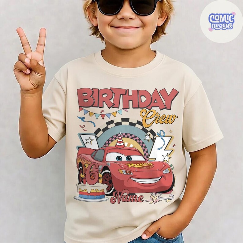 May include: Beige short-sleeve t-shirt with a graphic of a red race car and the text "BIRTHDAY Crew". The car has the number 6 on it and is decorated with a party hat. A birthday cake is also featured in the design.