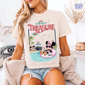 Puede incluir: Camiseta color crema con un dise&ntilde;o de Minnie Mouse en un flotador rosa, sosteniendo un helado. El dise&ntilde;o incluye las palabras "Disney Treasure", un crucero, palmeras y gaviotas.