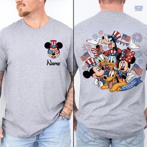 May include: A gray t-shirt featuring Mickey Mouse in patriotic attire with sunglasses and a hat. The text "Name" is below the graphic. The back of the shirt displays a group of Disney characters celebrating with flags and fireworks.