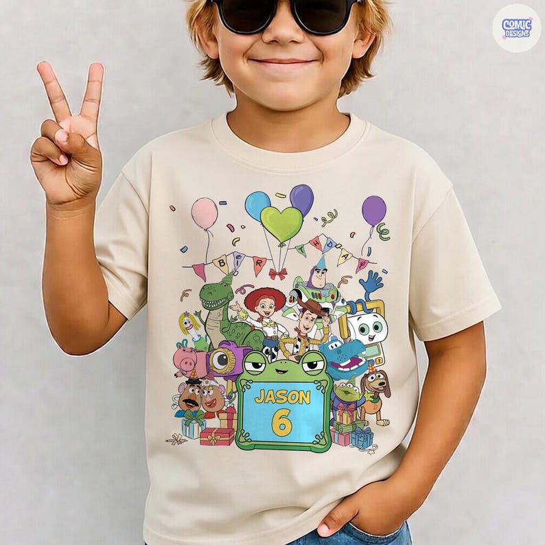 May include: A beige short-sleeve t-shirt featuring a colorful graphic of various animated toy characters, balloons, and a banner. A central green frame contains the text 'JASON' and the number '6' in yellow, surrounded by gift boxes.