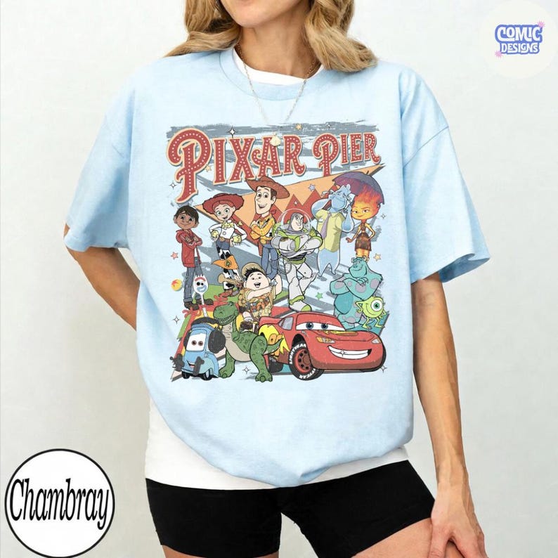Pu&ograve; includere: T-shirt azzurra con una grafica colorata dei personaggi di Pixar Pier. Il design include personaggi di Toy Story, Monsters, Inc., Cars e altro ancora. Il testo "Pixar Pier" &egrave; visualizzato in un font retr&ograve;. La maglietta ha maniche corte.