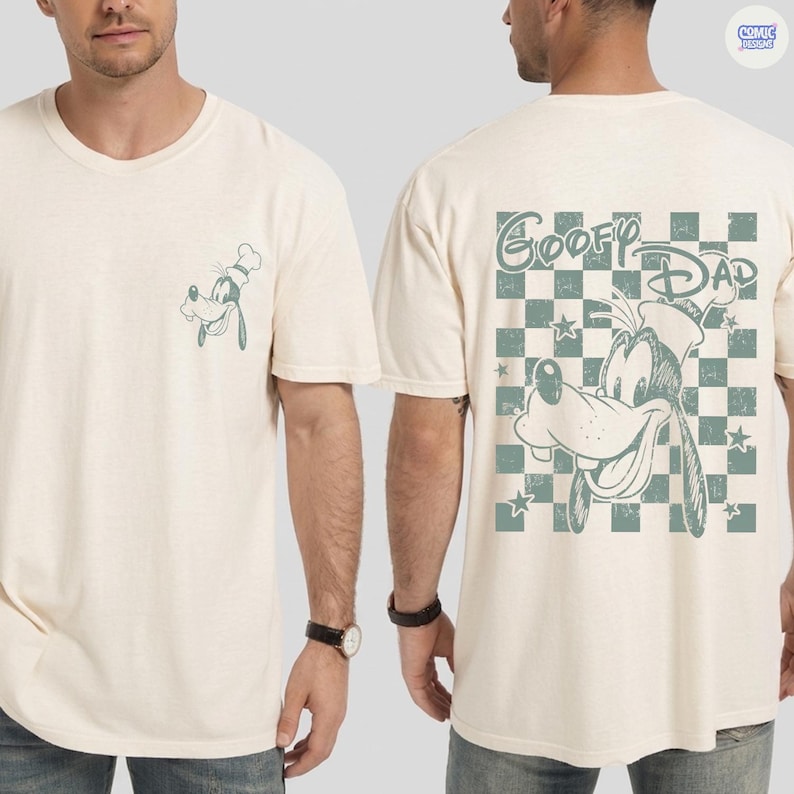 May include: Cream-colored t-shirt featuring a Goofy graphic on the front pocket and back. The back design includes the text "Goofy Dad" above a checkered pattern with stars. The shirt is a casual wear item.
