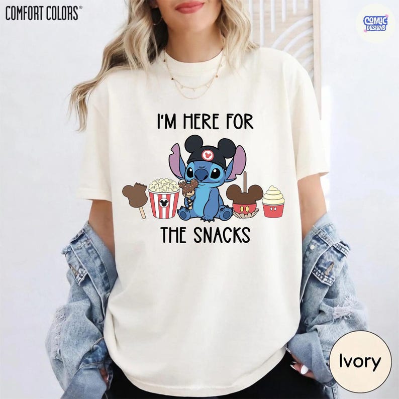 May include: Ivory-colored t-shirt with the text "I'M HERE FOR THE SNACKS" and a cartoon character wearing a hat and holding snacks. The shirt features a graphic of popcorn, a caramel apple, and a cupcake.