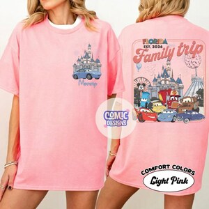 K&ouml;nnte beinhalten: Hellrosa T-Shirt mit einem Front-Design eines blauen Autos und Schlosses, mit dem Wort "Mommy". Auf der R&uuml;ckseite befindet sich ein "Florida Family Trip"-Design mit Zeichentrickfiguren und einem Schloss. Das Shirt ist mit "Comfort Colors Light Pink" gekennzeichnet.