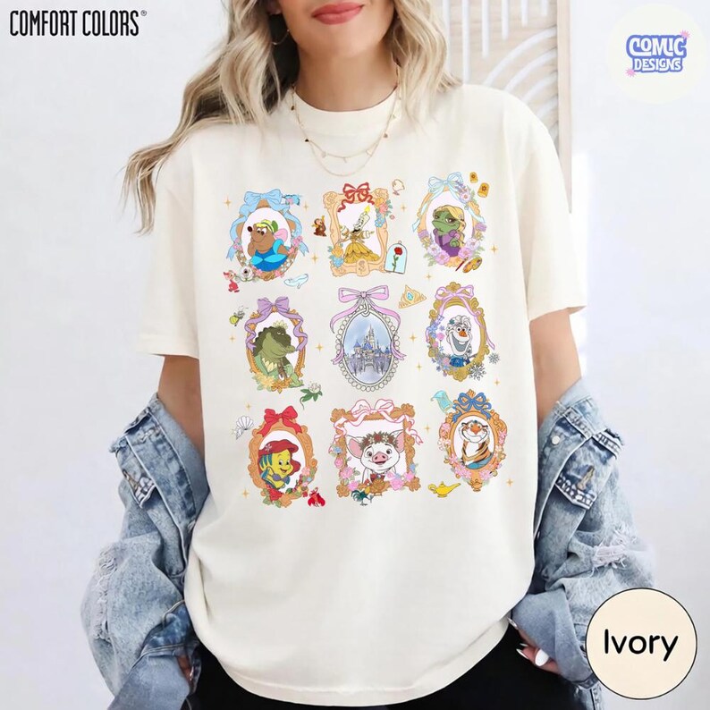 Puede incluir: Camiseta Comfort Colors color marfil con personajes de dibujos animados enmarcados. Los marcos dorados tienen lazos coloridos y detalles florales. El logotipo de Comic Designs est&aacute; en la esquina superior derecha. La camiseta es marfil.