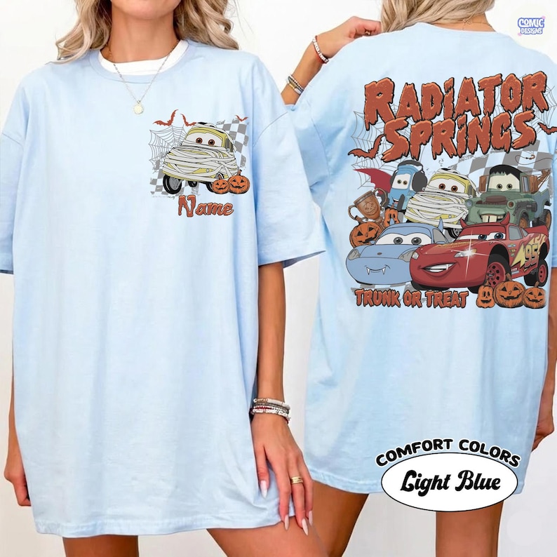 May include: A light blue t-shirt featuring a small graphic on the front chest of a mummy car with pumpkins and the word Name. The back displays a large graphic of multiple cartoon cars with Halloween themes, pumpkins, and the text Radiator Springs.