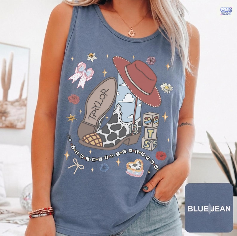 Puede incluir: Una camiseta sin mangas color azul jean con un estampado gr&aacute;fico de una bota vaquera con manchas de vaca, un sombrero vaquero rojo, un lazo rosa y bloques de letras T-S-S. El texto Taylor est&aacute; en la bota y I KNEW YOU aparece debajo.