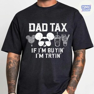 May include: Dark gray t-shirt with the text "DAD TAX" above a Mickey Mouse design wearing sunglasses and images of treats. Below the design is the text "IF I'M BUYIN' I'M TRYIN'".