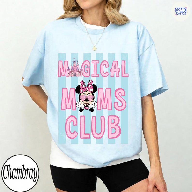 K&ouml;nnte beinhalten: Hellblaues T-Shirt mit dem rosa Text "MAGICAL MOMS CLUB", einer Minnie-Mouse-Grafik und einer Schlossillustration. Hinter dem Text befinden sich hellblaue vertikale Streifen. Das T-Shirt hat kurze &Auml;rmel.