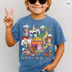 May include: Blue short-sleeve t-shirt featuring a colorful graphic of characters from the animated movie Toy Story. The text on the shirt reads "LIAM'S STORY" and "YOU'VE GOT A FRIEND WHO'S 7".
