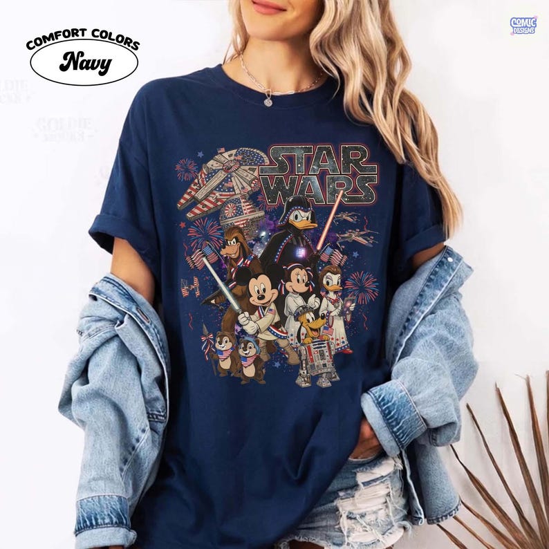 May include: Navy blue Comfort Colors t-shirt featuring a Star Wars graphic with various Disney characters, fireworks, and an American flag theme. The shirt has rolled-up sleeves and a crew neck.
