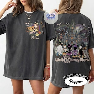 May include: A charcoal gray t-shirt featuring a front graphic of a character in a witch hat holding a pumpkin with the text Name. The back graphic displays a castle, bats, and cartoon characters in Halloween costumes with the text Walt Disney World.