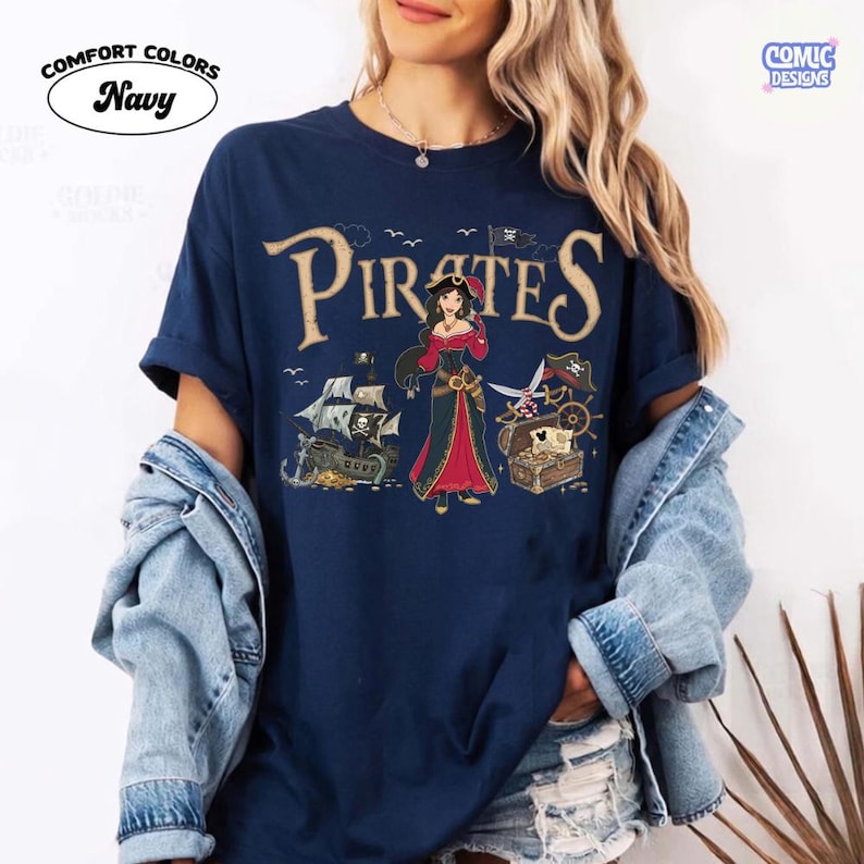 May include: Navy blue t-shirt with a pirate-themed graphic. The design features the word "Pirates" in gold lettering, a pirate ship, a treasure chest, and a female pirate character in red and black attire. The shirt has the words "Comfort Colors" and "Navy" printed on it.