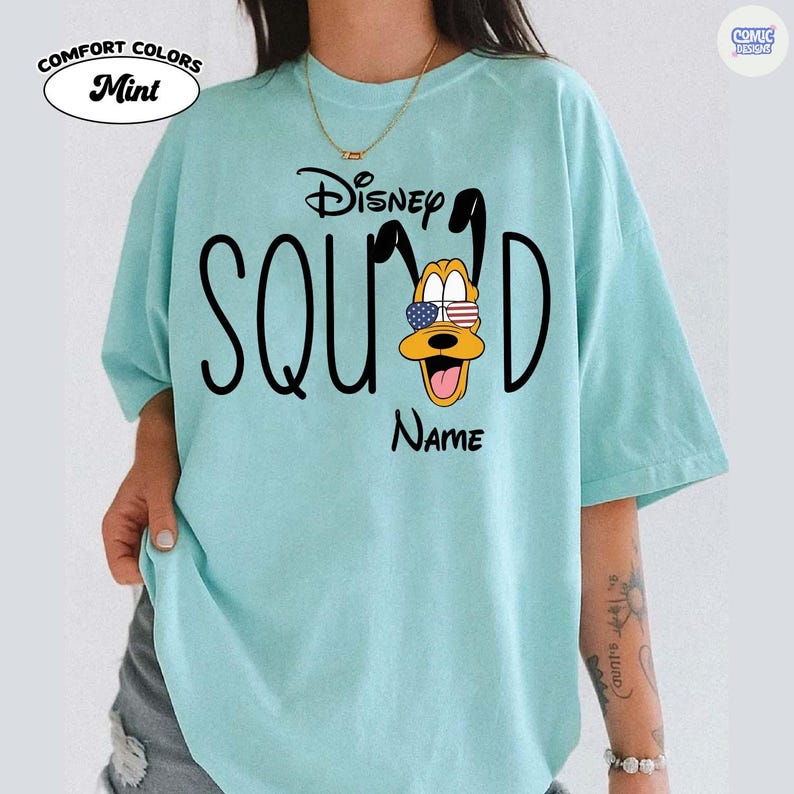 May include: Mint green t-shirt with the text "Disney Squad" and a Pluto graphic wearing American flag sunglasses. The shirt also has the word "Name" below the Pluto graphic. The shirt is a Comfort Colors brand.