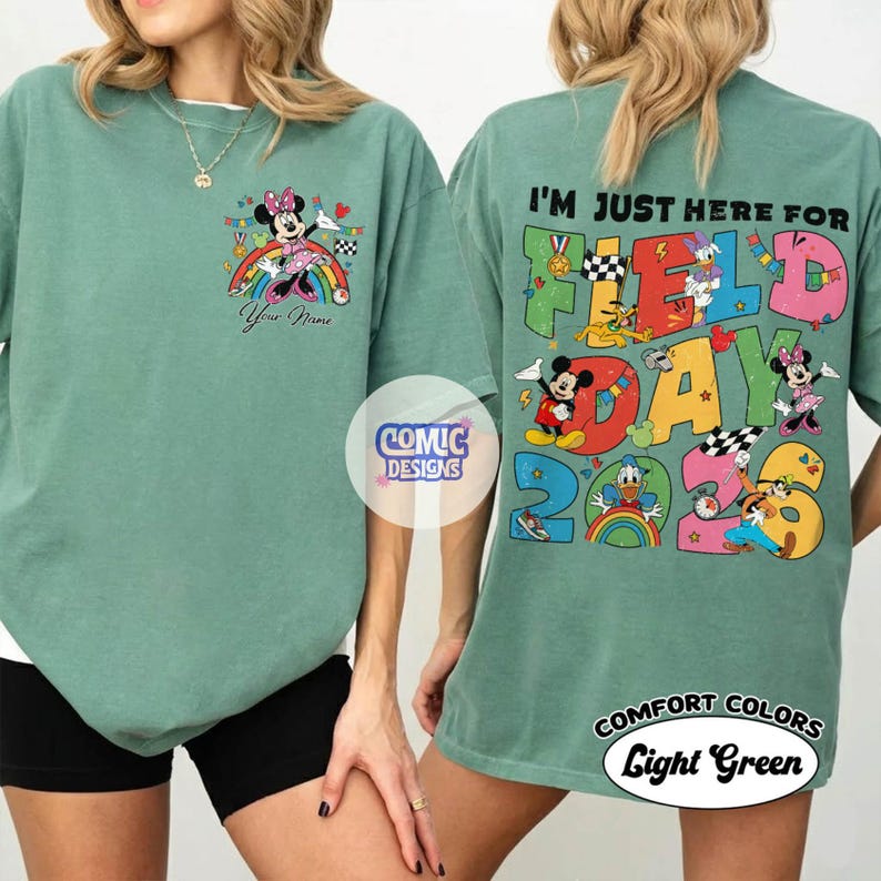 K&ouml;nnte beinhalten: Hellgr&uuml;nes T-Shirt mit einem Minnie Mouse-Motiv auf einem Regenbogen und dem Text "Your Name". Auf der R&uuml;ckseite steht "I'M JUST HERE FOR FIELD DAY 2023" mit Zeichentrickfiguren. Das T-Shirt ist hellgr&uuml;n.