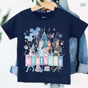 May include: Navy blue short-sleeve t-shirt with a colorful graphic featuring characters and elements from a popular animated movie. The design includes the text "Birthday Girl" and a number 5. The shirt is hanging on a wooden hanger.