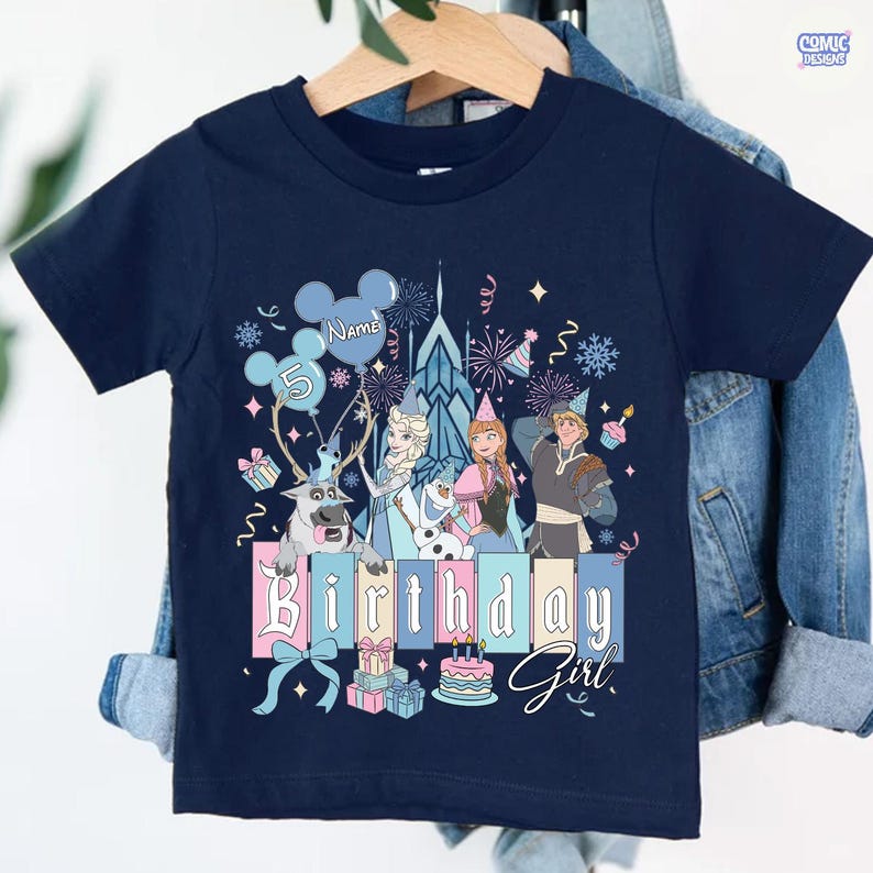 May include: Navy blue short-sleeve t-shirt with a colorful graphic featuring characters and elements from a popular animated movie. The design includes the text "Birthday Girl" and a number 5. The shirt is hanging on a wooden hanger.