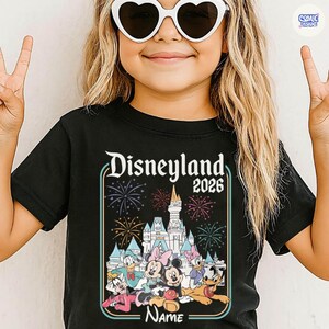 Op de afbeelding: Zwart T-shirt met een Disneyland-afbeelding met de tekst "Disneyland 2026". De afbeelding bevat tekenfilmfiguren zoals Mickey en Minnie Mouse, Donald Duck en vuurwerk. Onderaan de afbeelding is ruimte voor een naam.
