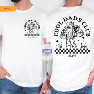 May include: White t-shirt with a black graphic on the front and back. The front graphic says "COOL DADS CLUB" with a cartoon character holding a beer mug. The back graphic is similar, with the text "#Levi".