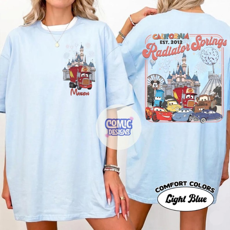 K&ouml;nnte beinhalten: Hellblaues T-Shirt mit einem Cartoon-Design eines roten Lastwagens und eines Schlosses, darunter der Name "Mason". Auf der R&uuml;ckseite des Shirts ist "California Radiator Springs" mit Cartoon-Autos und einem Schloss abgebildet. Das Shirt ist mit "Comfort Colors Light Blue" gekennzeichnet.