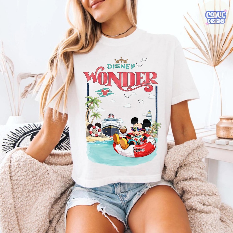 Puede incluir: Camiseta blanca con un dise&ntilde;o de Mickey Mouse con gafas de sol relaj&aacute;ndose en una boya roja y blanca. El dise&ntilde;o incluye las palabras "Disney Wonder" en rojo, un crucero, palmeras y un faro.