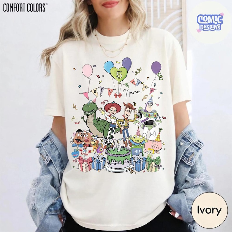 Puede incluir: Una camiseta de manga corta color marfil con un gr&aacute;fico colorido de varios personajes de juguetes animados, un pastel de cumplea&ntilde;os con el n&uacute;mero cinco, globos y confeti. El texto "Birthday" y "Name" est&aacute; impreso sobre los personajes.