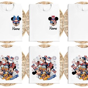May include: White t-shirts featuring patriotic Disney characters. Designs include Mickey and Minnie Mouse, Donald Duck, and Pluto in red, white, and blue attire. Some shirts have the word "Name" printed below the character.