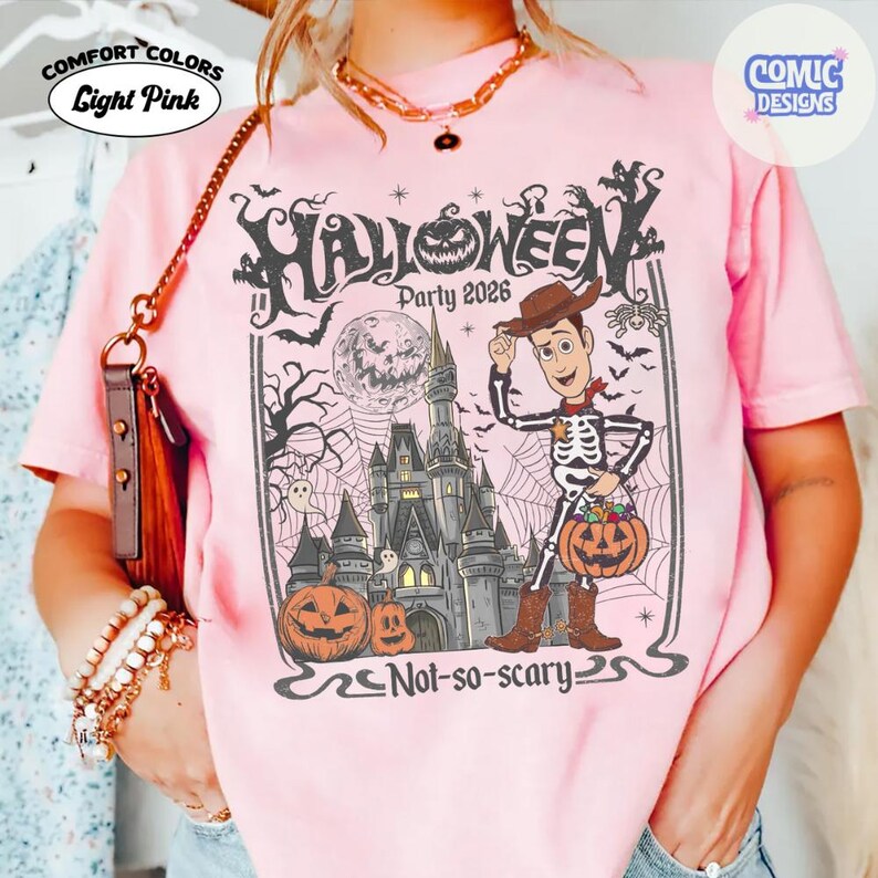 Puede incluir: Una camiseta rosa claro con un estampado gr&aacute;fico negro con el texto Halloween Party 2026 y Not-so-scary. El dise&ntilde;o incluye un personaje de dibujos animados vestido de esqueleto, un gran castillo, una calabaza, luna llena y telara&ntilde;as.