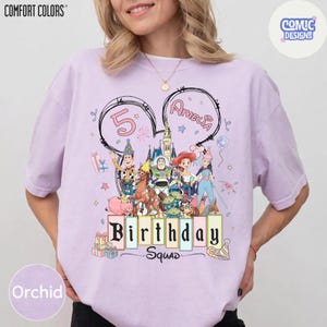 May include: Orchid-colored t-shirt with a graphic featuring Disney characters, the number 5, and the name "Amelia" in a Mickey Mouse ear design. The text "Birthday Squad" is also displayed. The shirt is from Comfort Colors.