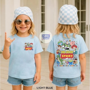 May include: A light blue t-shirt featuring a small Toy Story character graphic on the front with the name EMILY and a large, detailed Toy Story character graphic on the back with the text 2ND GRADE STORY TO 2ND GRADE AND BEYOND.