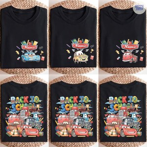 May include: A black t-shirt featuring a graphic print of various cartoon cars and school supplies. The design includes the text "Name" on a sign above a car, and the text "BACK TO SCHOOL" with multiple vehicles and school-themed icons.