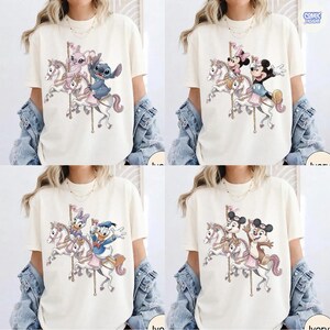 May include: Ivory-colored t-shirts featuring cartoon characters on a carousel. The designs include Stitch and Angel, Mickey and Minnie Mouse, Donald and Daisy Duck, and Chip and Dale. The shirts have a classic, casual style.