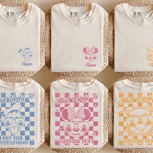 May include: Six off-white t-shirts with cartoon character designs. The top row features characters with the word "Name" below. The bottom row has the text "Most Likely To" and "Pay For Everything" or "Custom Text".