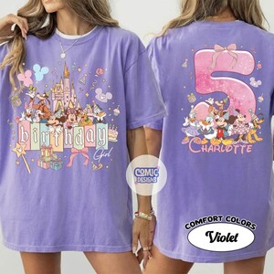 May include: A violet-colored t-shirt featuring a birthday design with cartoon characters and the text "Birthday Girl" on the front. The back of the shirt displays a large number "5" with a bow and the name "Charlotte".