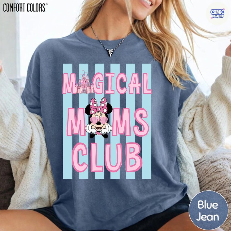 K&ouml;nnte beinhalten: Blaues Comfort Colors Sweatshirt mit dem Text "MAGICAL MOMS CLUB" in Rosa, mit Minnie Mouse und einer Schlossgrafik. Das Design ist vor einem hellblau gestreiften Hintergrund platziert.