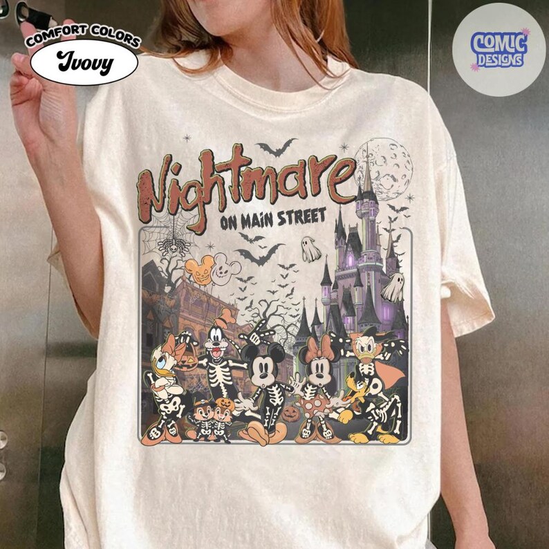 May include: An ivory t-shirt featuring a graphic print with the text Nightmare on Main Street. The design includes cartoon characters wearing skeleton costumes in front of a castle, a full moon, bats, ghosts, and a spiderweb in a vintage style.