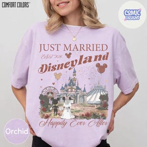 May include: Orchid-colored t-shirt with a Disneyland graphic. The design includes the text "Just Married Disneyland Est 2026" with Mickey and Minnie Mouse, a castle, and the words "Happily Ever After".