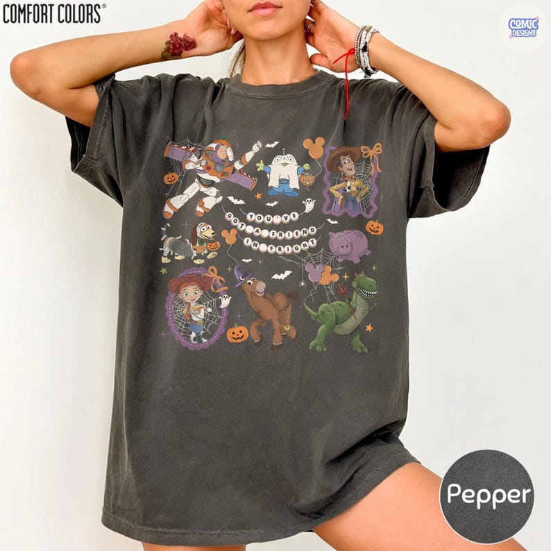 May include: A charcoal gray short-sleeve t-shirt featuring a Halloween-themed graphic with various cartoon characters, spiderwebs, pumpkins, and the text "YOU'VE GOT A FRIEND IN FRIGHT" arranged in the center. The shirt has a relaxed, loose fit.