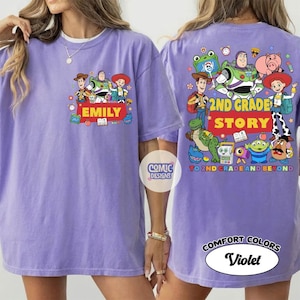 May include: A light purple t-shirt featuring Toy Story characters. The front shows Woody, Buzz Lightyear, and Jessie with the name EMILY. The back displays the same characters with the text 2ND GRADE STORY TO 2ND GRADE AND BEYOND.