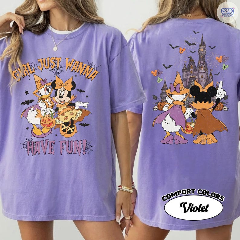 May include: A violet t-shirt featuring a front graphic of Daisy Duck and Minnie Mouse in Halloween costumes with the text "GIRL JUST WANNA HAVE FUN!" and a back graphic showing the characters facing a castle with bats and pumpkins.