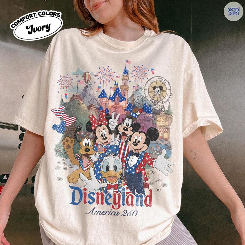 Puede incluir: Una camiseta de manga corta color marfil con un gr&aacute;fico de Mickey Mouse, Minnie Mouse, el Pato Donald y Pluto con vestimenta patri&oacute;tica. El dise&ntilde;o incluye un castillo, fuegos artificiales y el texto Disneyland America 250 en fuente roja y azul desgastada.