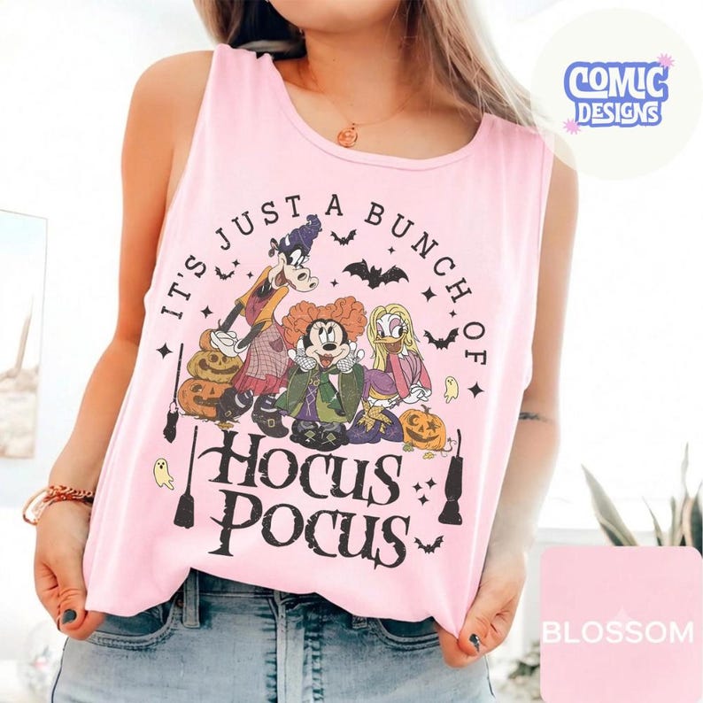 May include: A light pink sleeveless tank top featuring a graphic print of three cartoon characters dressed as witches. The text reads IT'S JUST A BUNCH OF HOCUS POCUS. The design includes pumpkins, bats, and broomsticks in black, orange, and purple tones.