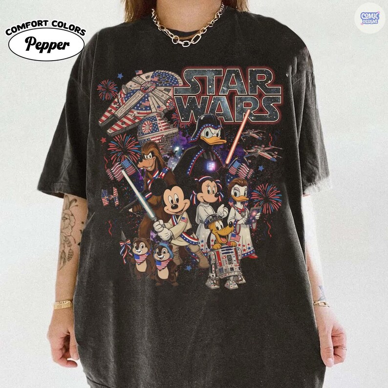 May include: Dark gray Comfort Colors t-shirt featuring a Star Wars graphic with Disney characters. The design includes Darth Vader, Mickey Mouse, Donald Duck, and fireworks with American flag elements. The shirt has the text "STAR WARS".